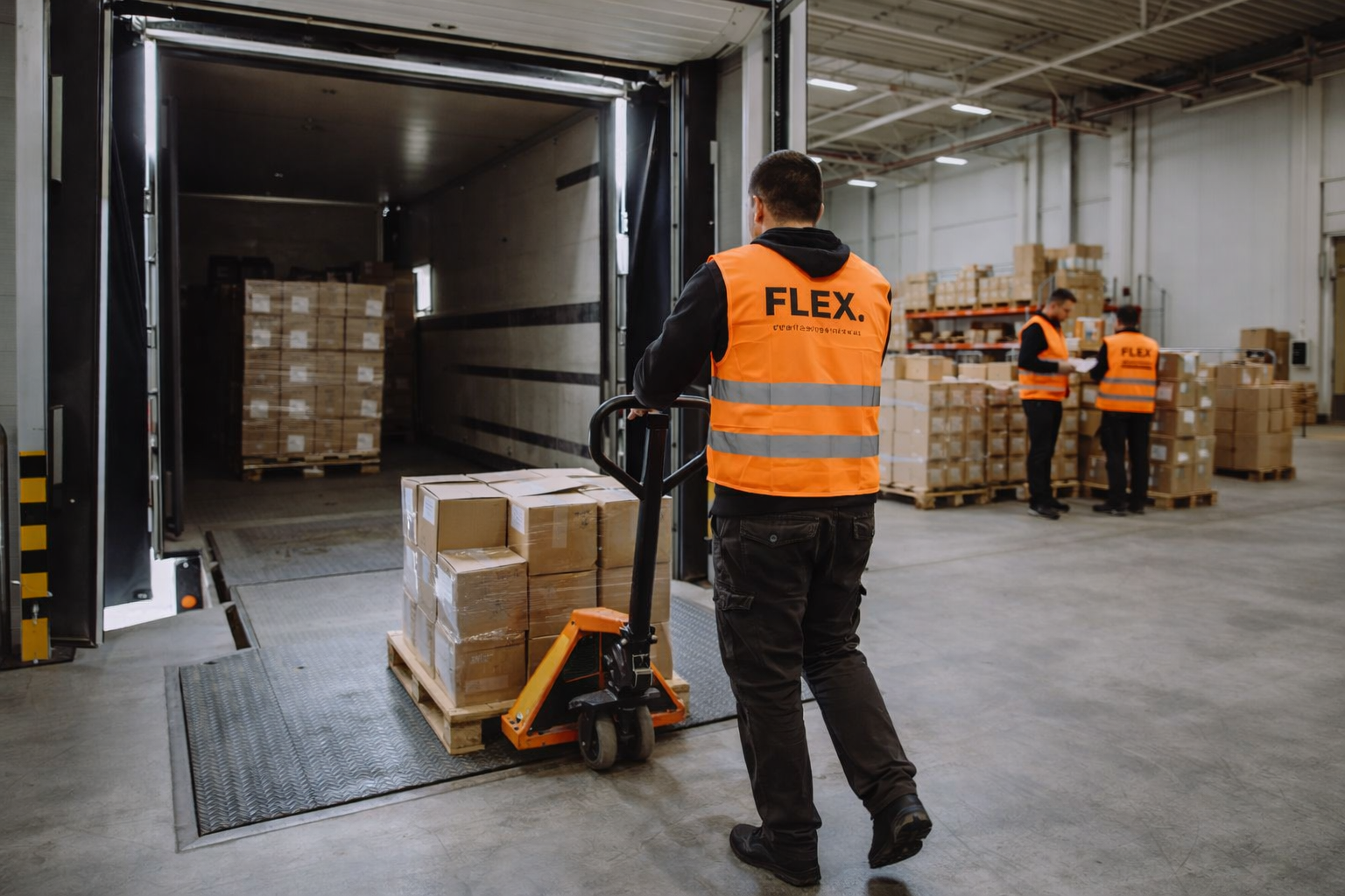 FLEX. warehouse worker moving inbound goods from a delivery truck across a loading dock with a hand pallet jack