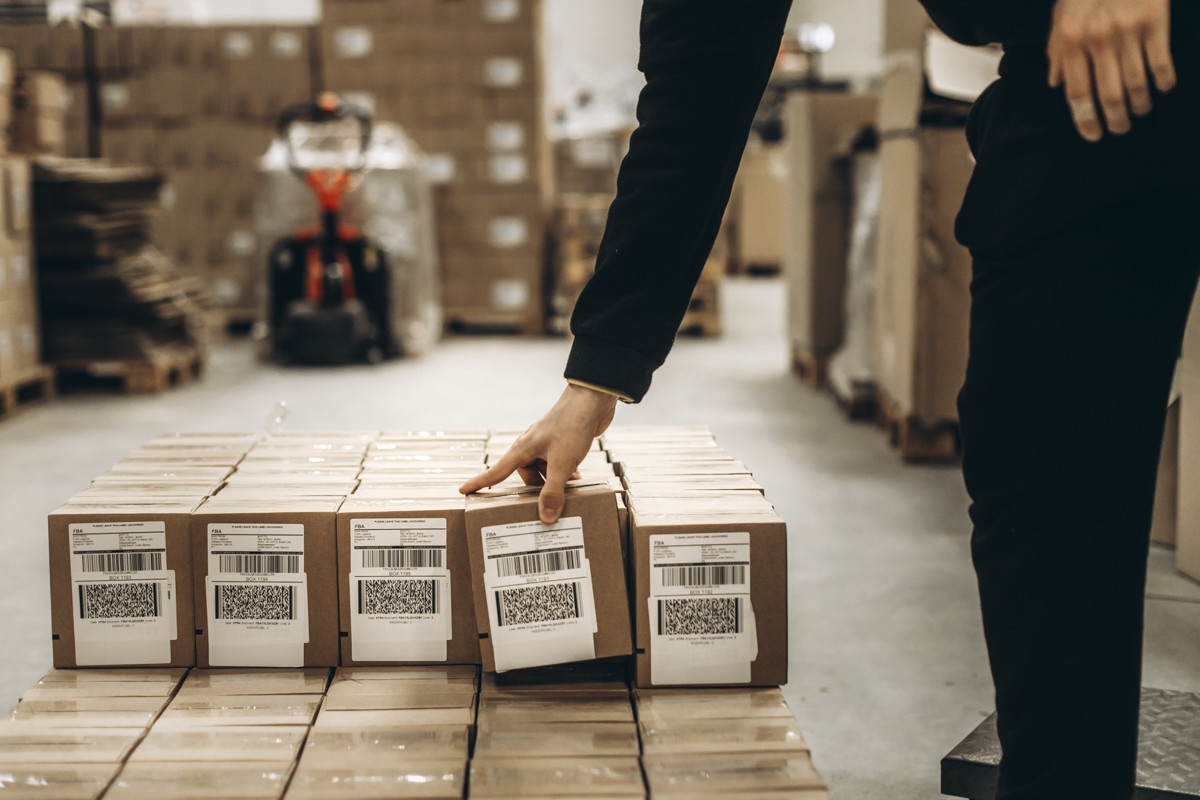 Warehouse employee checking labeled cartons arranged on a pallet, with barcode and FBA shipping labels visible on the front of each box.